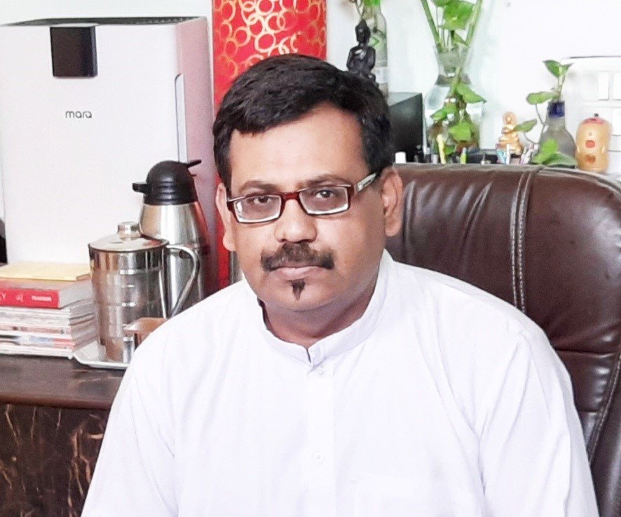 Woman with long light brown hair pinching the bridge of her nose with eyes closed, wearing a light pink top, against a light gray background